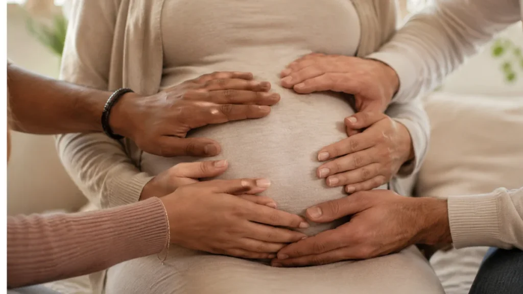 Barriga de gestante cercada por várias mãos, representando acolhimento e rede de apoio na maternidade.